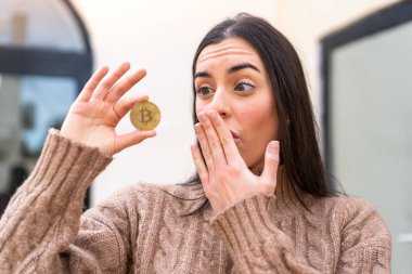 Dışarıda Bitcoin tutan genç bir kadın. Şaşırmış ve şok olmuş bir yüz ifadesi var.