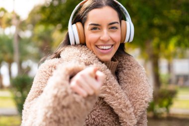 Genç esmer kadın açık havada müzik dinliyor.