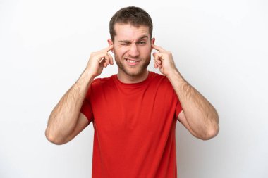 Beyaz arka planda izole edilmiş genç beyaz adam hayal kırıklığına uğramış ve kulaklarını kapatmış.
