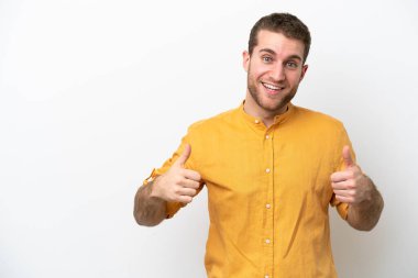 Beyaz arka planda izole edilmiş genç beyaz bir adam baş parmak hareketi yapıyor.