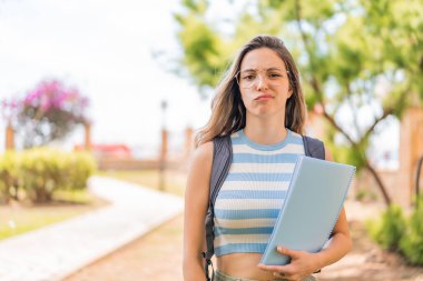 Dışarıda üzgün bir ifadeyle genç ve güzel bir bayan öğrenci.