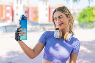 Dışarıda bir şişe su ve üzgün bir ifadeyle genç ve güzel bir bayan.