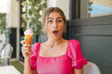 Açık havada kornet dondurmalı genç sarışın kadın. Şaşırmış ve şok olmuş bir yüz ifadesi var.