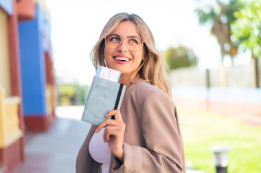 Sarışın, güzel, Uruguaylı bir kadın açık havada elinde mutlu bir ifadeyle pasaport tutuyor.