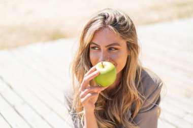 Sarışın, güzel bir Uruguaylı kadın açık havada elma tutuyor.