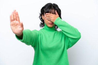 Beyaz arka planda izole edilmiş genç Arjantinli kadın jesti durdurup yüzünü kapatıyor.