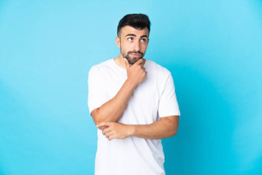 İzole edilmiş mavi arka plan üzerinde beyaz bir adam yukarı bakarken bir fikir düşünüyor.