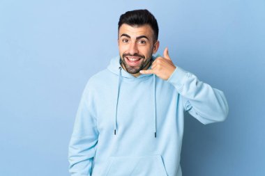 İzole edilmiş mavi arka planda beyaz bir adam telefon jesti yapıyor. Bana geri dönüş işareti ver.