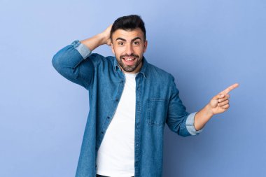 İzole edilmiş mavi arka planı olan beyaz bir adam şaşırdı ve parmağını yana çevirdi.