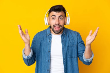 İzole edilmiş sarı arka planı olan beyaz bir adam şaşırdı ve müzik dinliyor.