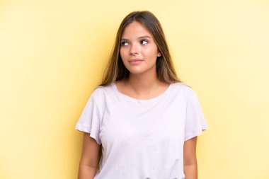 Sarı arka planda izole edilmiş genç beyaz kadın şüpheli hareketler yapıyor.