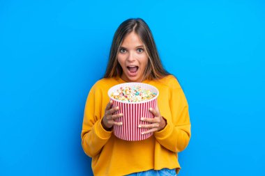 Mavi arka planda izole edilmiş beyaz bir kadın elinde koca bir kova patlamış mısır tutuyor.
