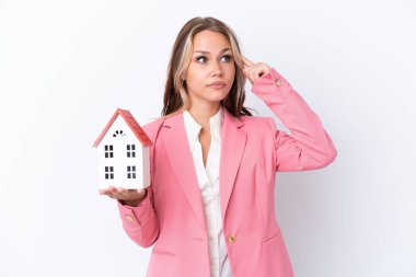 Rus emlakçı, beyaz arka planda izole edilmiş bir oyuncak evi tutuyor. Şüpheleri var ve düşünüyor.