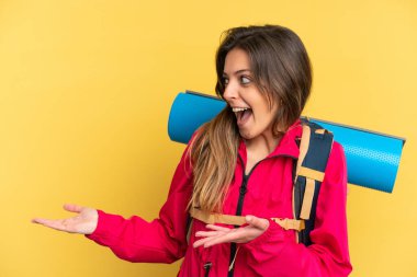 Young mountaineer man with a big backpack isolated on yellow background with surprise expression while looking side