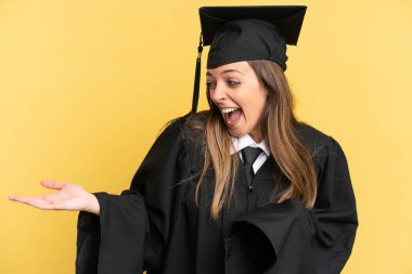 Genç üniversite mezunu, sarı arka planda tek başına, sürpriz bir ifadeyle yan yana bakarken.