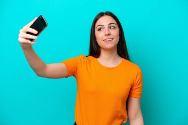 Mavi arka planda izole edilmiş beyaz bir kadın selfie çekiyor.