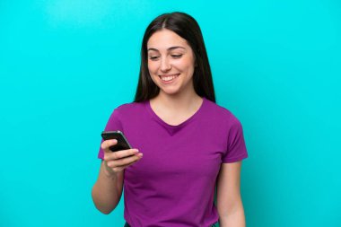 Mavi arkaplanda izole edilmiş genç bir kız cep telefonuyla bir mesaj ya da e-posta gönderiyor