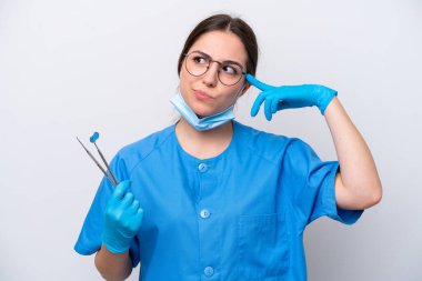Beyaz arka planda izole edilmiş aletleri tutan beyaz dişçi kadının şüpheleri ve düşünceleri var.