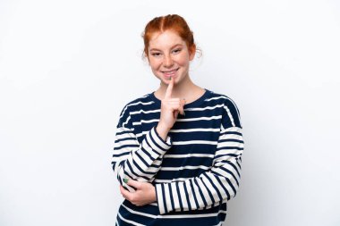 Beyaz arka planda izole edilmiş genç kızılımsı bir kadın sessizce hareket ettiğini gösteriyor. Parmağını ağzına sokuyor.