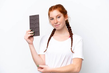 Young reddish woman isolated on white background taking a chocolate tablet and happy