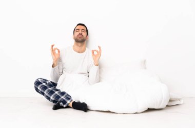 Beyaz, pijamalı bir adam. Zen pozisyonunda yerde oturuyor.