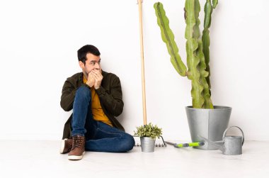 Bahçıvan içeride yerde oturuyor ağzını kapatıyor ve yan tarafa bakıyor.