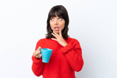 Beyaz arka planda izole edilmiş bir fincan kahve tutan beyaz bir kadın yukarı bakarken şüpheleri var.