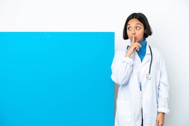 Beyaz arka planda izole edilmiş büyük bir pankartla genç melez doktor kadın parmağını ağzına koyan sessizlik işareti gösteriyor.