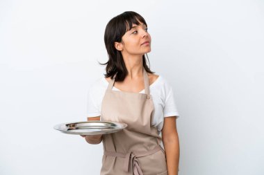 Tepsisi beyaz arka planda olan genç garson yan tarafa bakıyor.