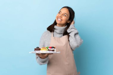 Pasta şefi büyük bir pastayı izole edilmiş mavi arka planda tutarak bir fikir düşünüyor..