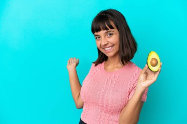 Mavi arka planda avakado tutan genç bir ırk kadını davet etmek için ellerini yana uzatıyor.