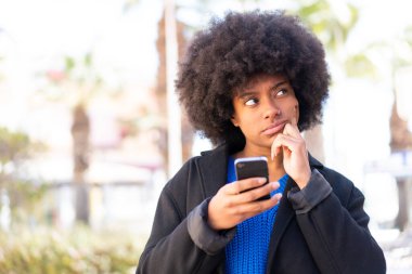 Açık havada cep telefonu kullanan ve düşünen Afrikalı Amerikalı bir kız.