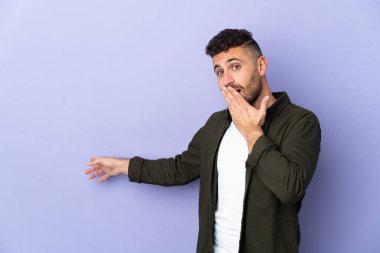 Caucasian man isolated on purple background with surprise expression while pointing side clipart