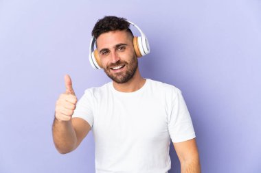Mor arka planda izole edilmiş beyaz bir adam müzik dinliyor ve başparmağını kaldırıyor.