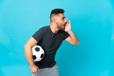 Futbolcu mavi arka planda izole edilmiş ve ağzı sonuna kadar açık bağırıyor.