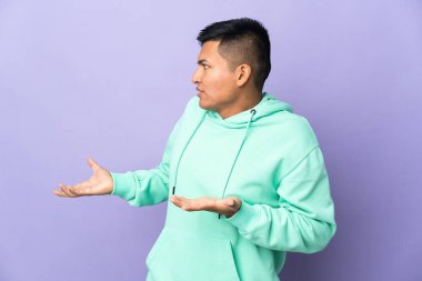 Young Ecuadorian man isolated on purple background with surprise expression while looking side