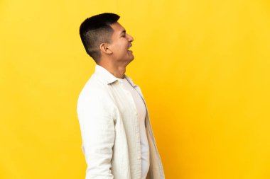 Genç Ekvadorlu adam sarı arka planda izole edilmiş. Yan pozisyonda gülüyor.