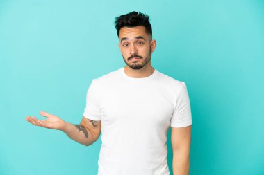 Mavi arka planda izole edilmiş genç beyaz adam şüpheli hareketler yapıyor.