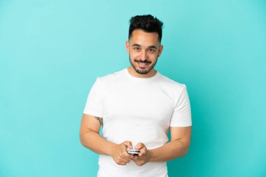 Mavi arka planda izole edilmiş genç beyaz adam cep telefonuyla bir mesaj gönderiyor.