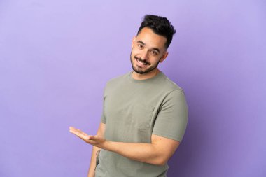 Mor arka planda izole edilmiş genç beyaz adam gülümserken bir fikir sunuyor.