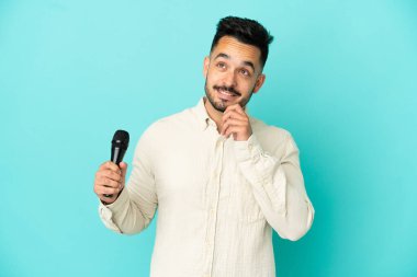 Kafkasyalı genç şarkıcı mavi arka planda izole edilmiş bir şekilde yukarı bakarken bir fikir düşünüyor.