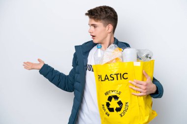 Beyaz arka planda sürpriz bir ifadeyle geri dönüşüm yapmak için elinde plastik şişelerle dolu bir çanta tutan Rus ergen.