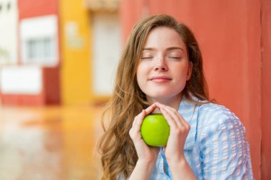 Açık havada elinde elma tutan kızıl saçlı genç bir kadın.