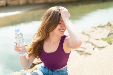 Açık havada elinde bir şişe su olan genç kızıl kadın bir şeyin farkına vardı ve çözümü arıyor.