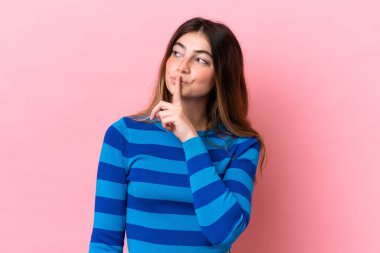 Pembe arka planda izole edilmiş beyaz bir kadın sessiz bir jest işareti gösteriyor. Parmağını ağzına sokuyor.