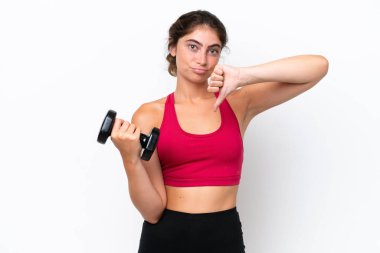 Beyaz arka planda izole haldeyken ağırlık kaldıran genç beyaz kadın olumsuz bir ifadeyle baş parmağını aşağı gösteriyor