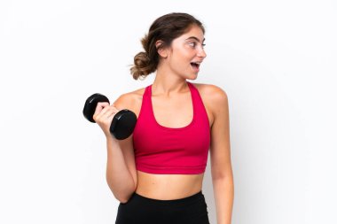 Beyaz arka planda izole haldeki beyaz kadın halter kaldırıyor. Yan pozisyonda gülüyor.