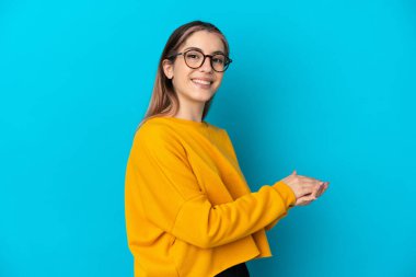 Mavi arka planda izole edilmiş genç beyaz kadın alkışlıyor.