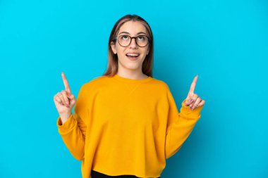 Mavi arka planda izole edilmiş genç beyaz kadın şaşırmış ve yukarı bakıyor.