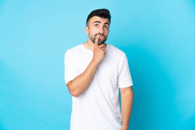 İzole edilmiş mavi arka planı olan beyaz bir adam yukarı bakarken şüpheleri var.